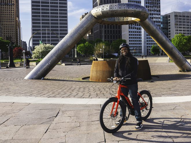 Jason Hall standing with Super Commuter+ beside Detroit fountain.