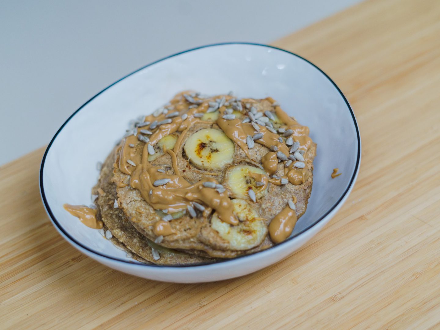 Bowl with banana pancakes topped with seeds, banana slices and peanut butter