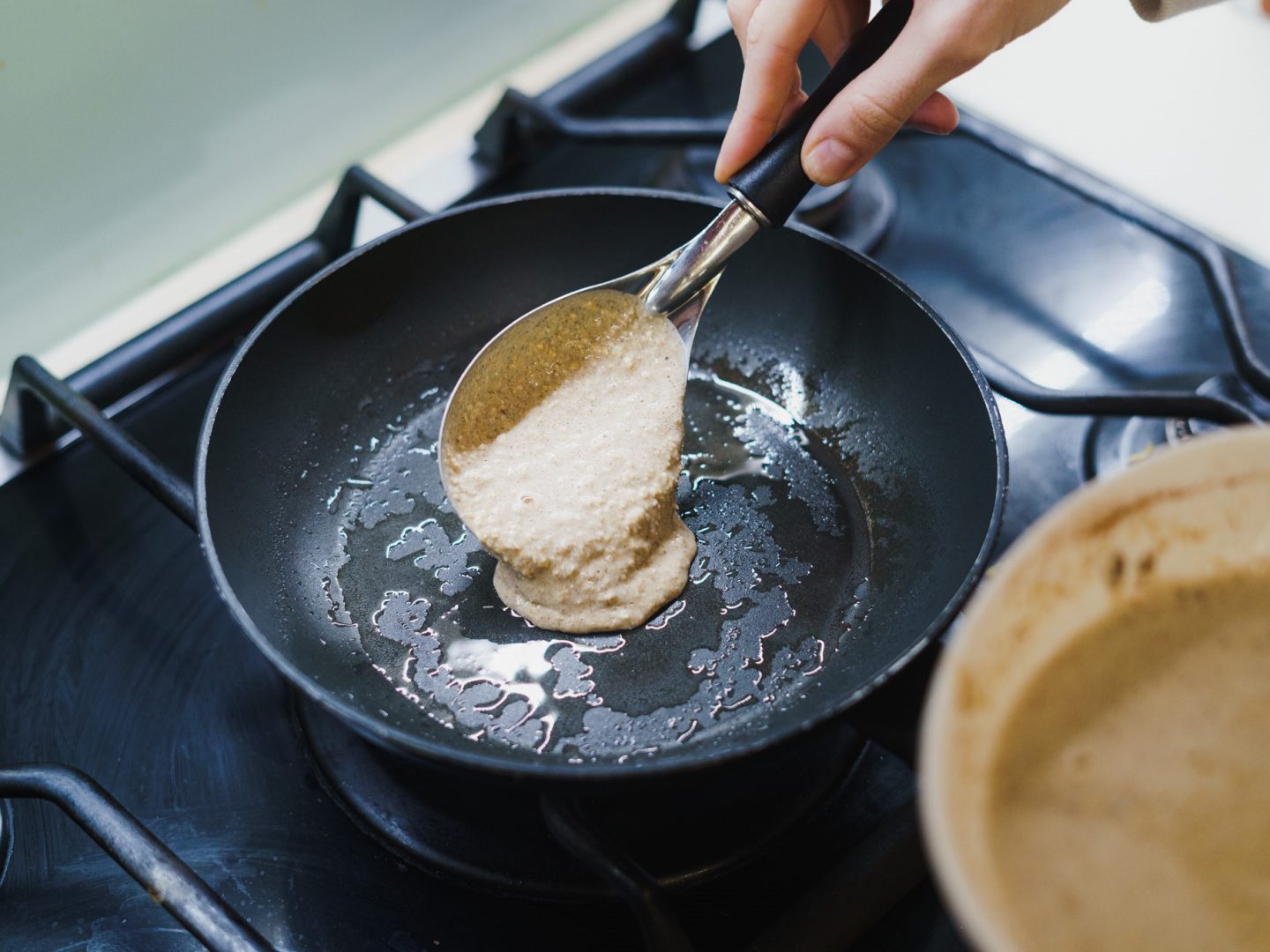 Skillet on stove with banana pancake mixture being poured in
