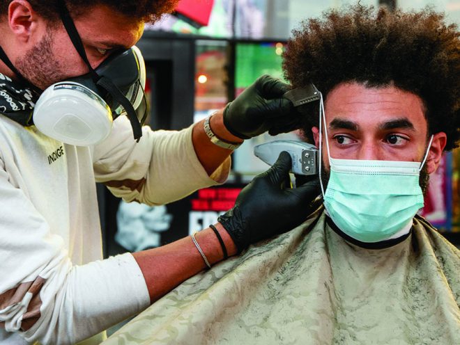 Julien Howard, The Velo Barber, trimming a man’s sideburns outside in Times Square while wearing gloves and a face mask.