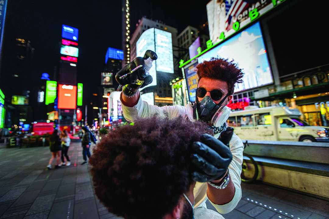 Käsineitä ja kasvosuojainta käyttävä The Velo Barber muotoilee asiakkaan hiuksia Times Squarella, jossa ei ole lähes lainkaan autoja tai jalankulkijoita.