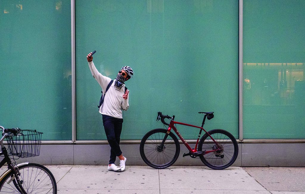 Julien Howard aka The Velo Barber taking a selfie on the sidewalk in front of a glass building with his Trek Checkpoint.