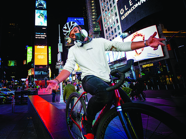 Julien Howard com os braços abertos na Times Square à noite, se equilibra em sua bicicleta Trek.