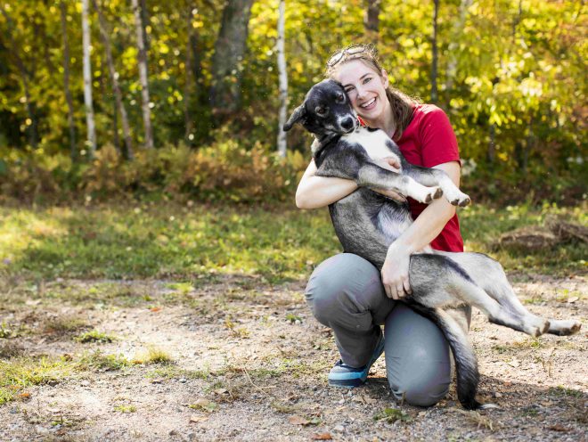 Blair Braverman sonríe y abraza a uno de sus perros en un sendero.