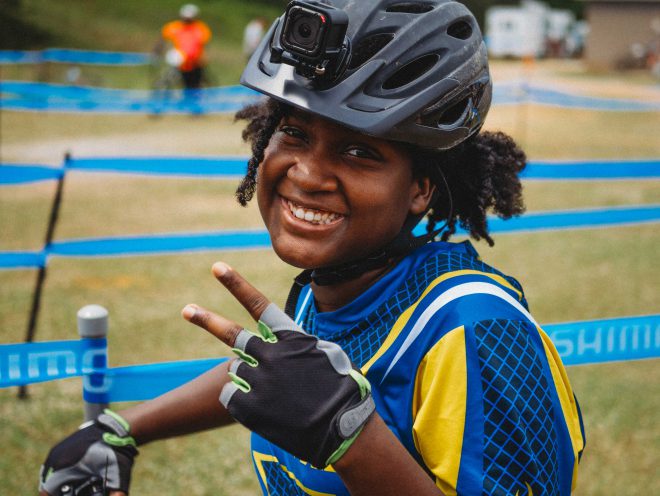 NICA student-athlete wearing a bike helmet, smiling and gesturing to the camera.