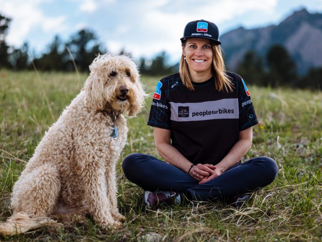 Jenn Dice, junto a su perro, sentada en la hierba.