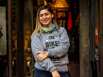 Mulher (Tati Koufopanteli) em frente a uma loja de bicicletas