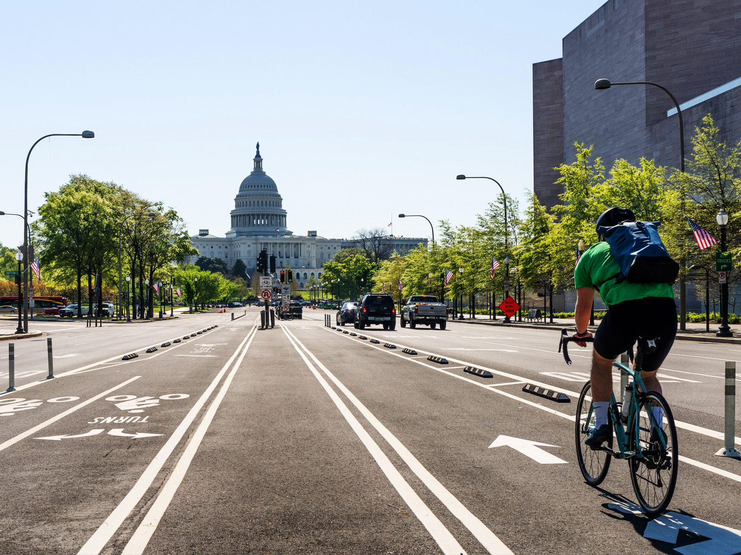 In the foreground a cyclist wearing a green shirt and black shorts rides down Pennsylvania Ave toward the White House.