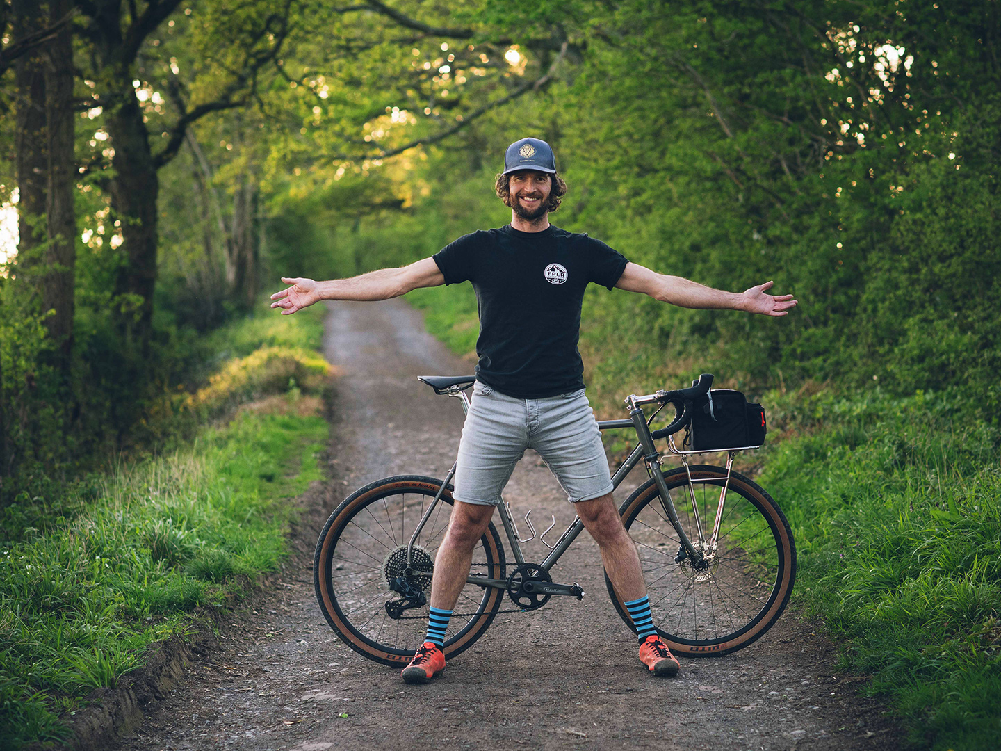 Wayne Reid parado delante de su bicicleta en una pista de tierra arbolada