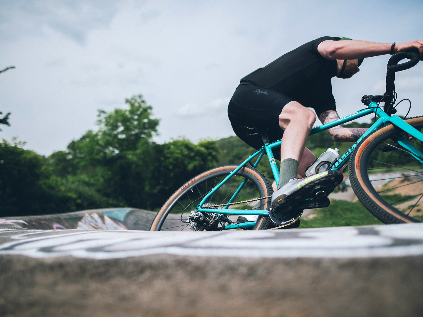 Ciclista numa bicicleta de gravel num circuito pump track repleto de graffiti.