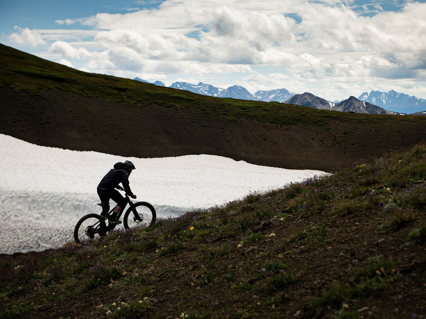 Biker fährt neben einem Schneefeld einen Trail hoch
