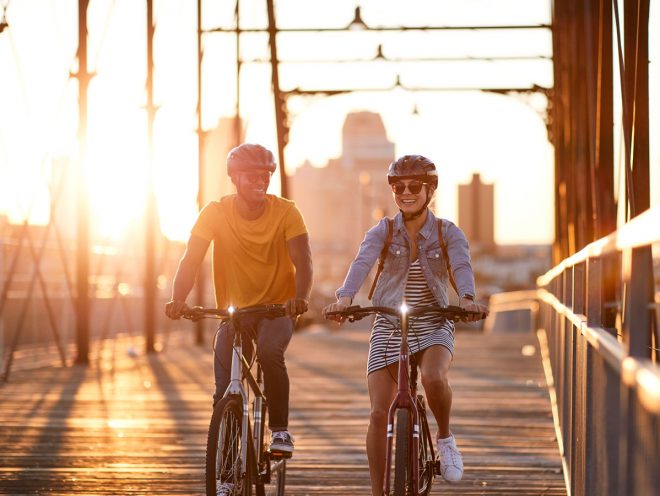 Un hombre y una mujer cruzando un puente en bici al atardecer