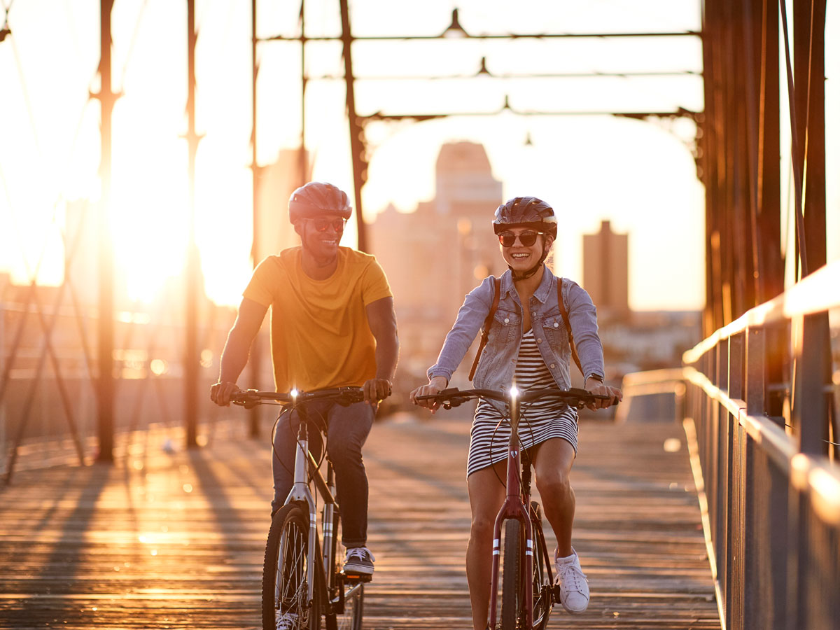 A man and a woman ride bikes across a bridge at sunset
