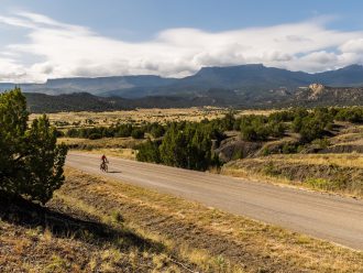 Un cycliste sur un sentier gravel et des montagnes en arrière-plan.