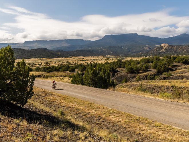 A rider on a gravel road and mountains in the background.