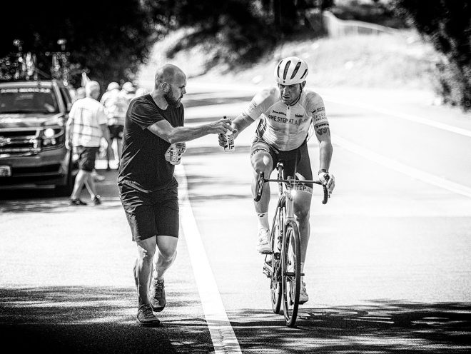 James is handed a water bottle while riding his bike.