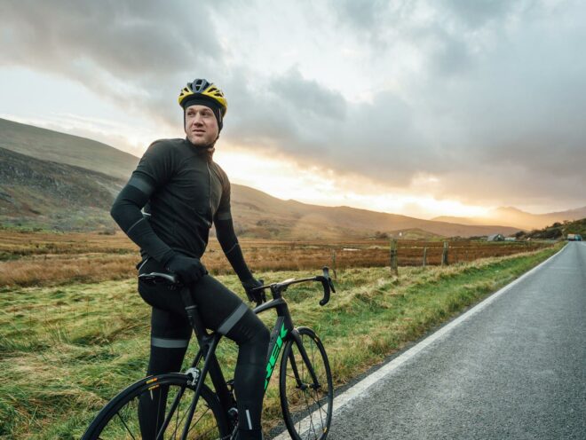 James Golding está sobre su bicicleta a la orilla de la carretera mirando hacia atrás.
