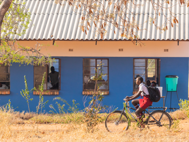 Pige i skoleuniform cyklende på en Buffalo-cykel forbi et blåt hus.