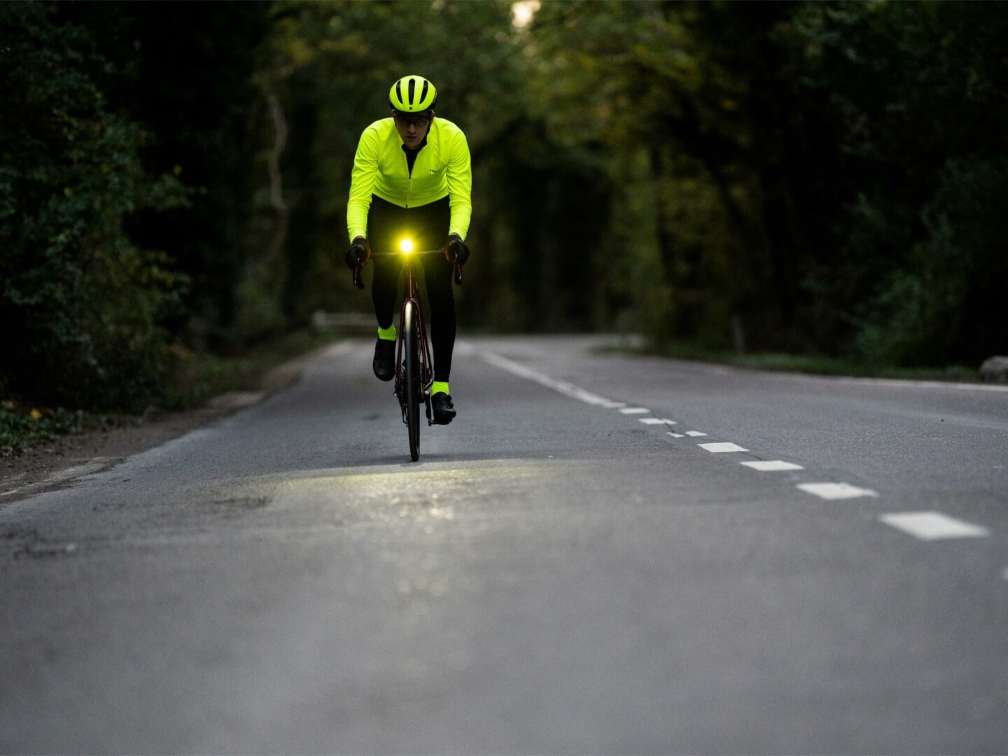 En cyklist som cyklar vid sidan av en landsväg i mörkret