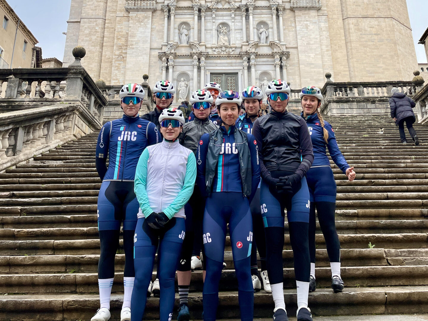 Team members of the JRC Women's Junior Cycling Team stand together on ancient stone steps in Girona.