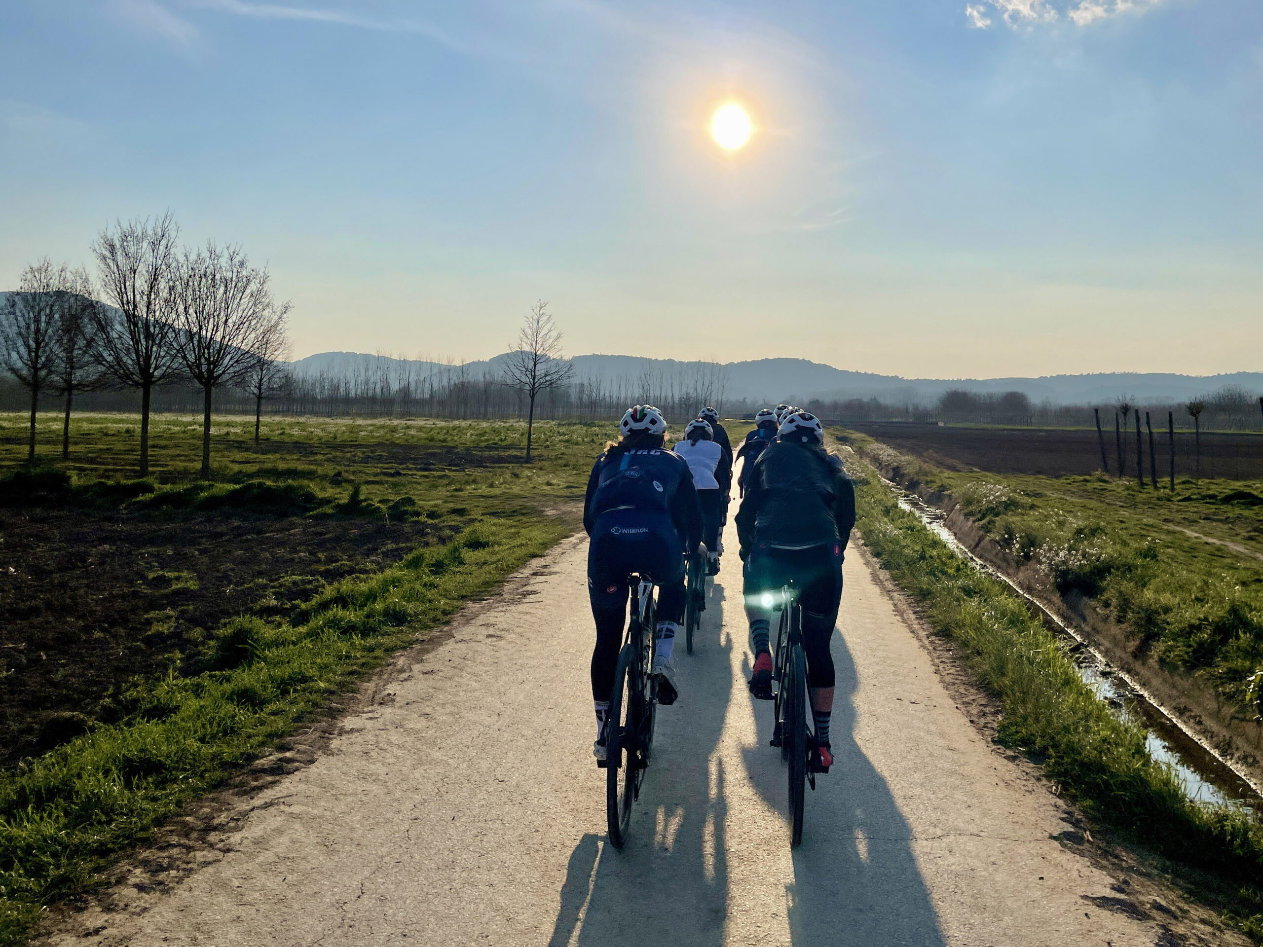 A team rides away from the camera on a dirt road in the Girona countryside.