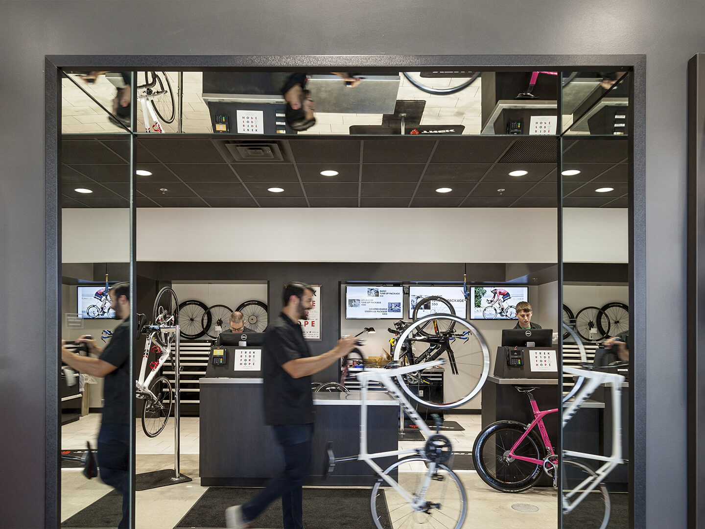 Inside the front doors of a Trek bike shop with an employee rolling a bike past the entryway.