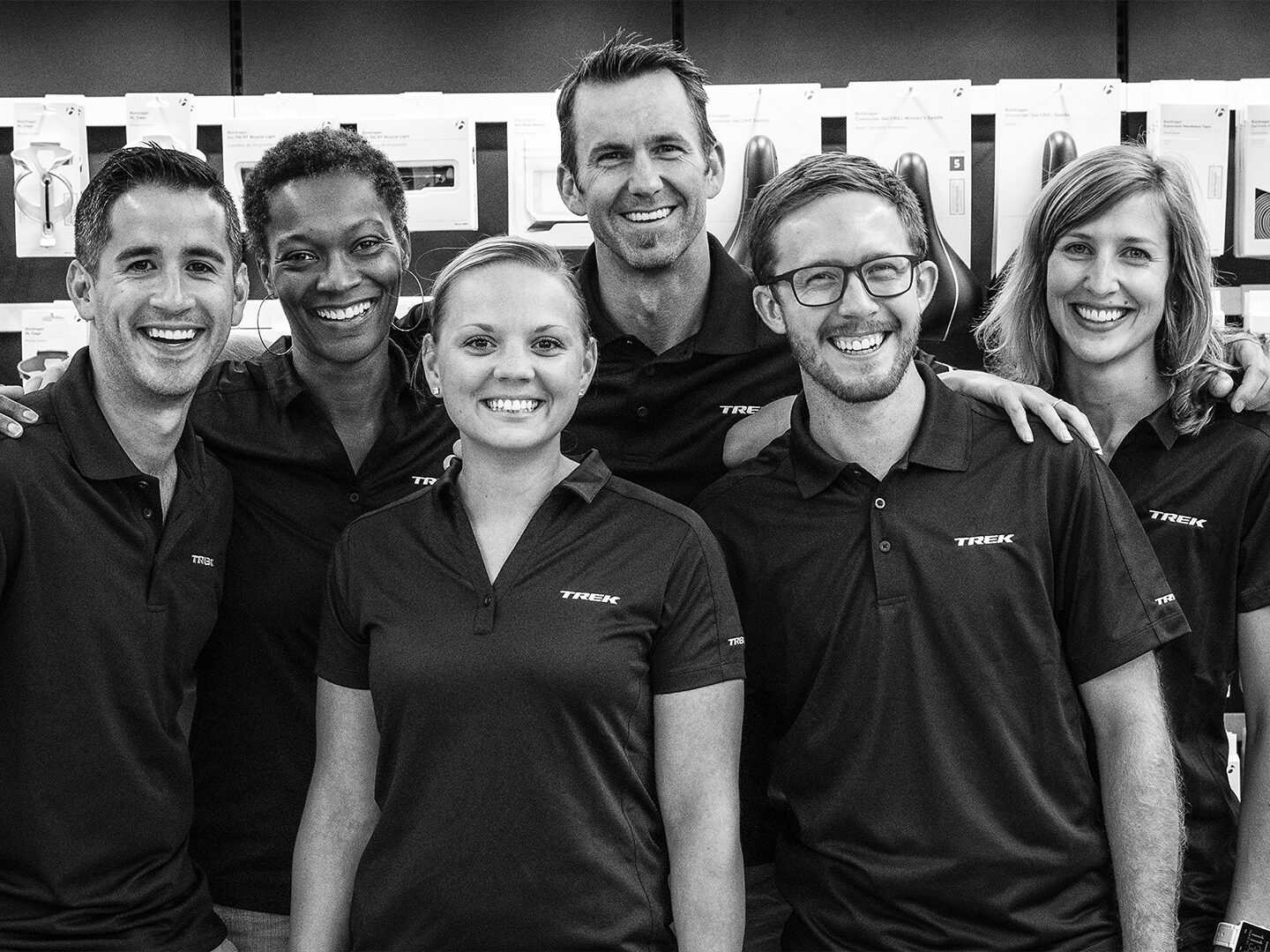 A black and white photo of six Trek employees standing together and smiling in work polos.