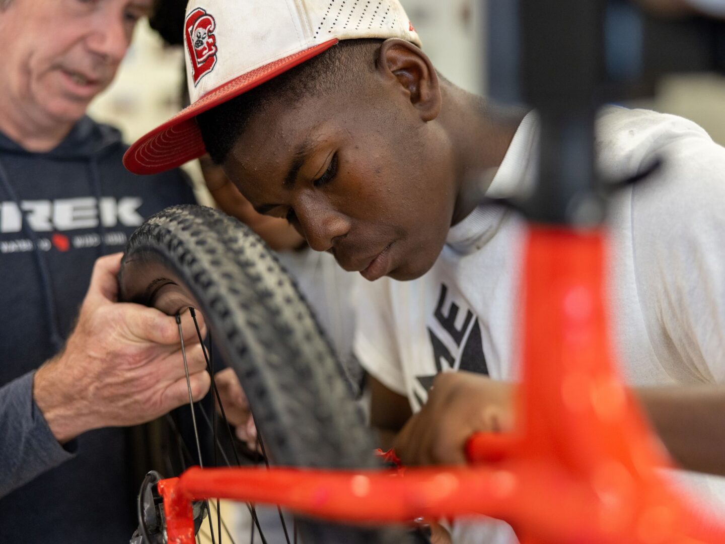 A boy fixing something on a rear bike wheel with the help of a man in a Trek sweatshirt.