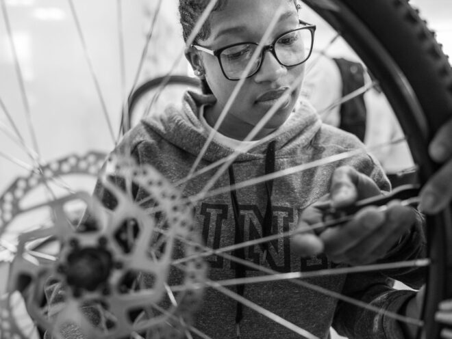 A through-the-spokes shot of a young girl working on a bike wheel.