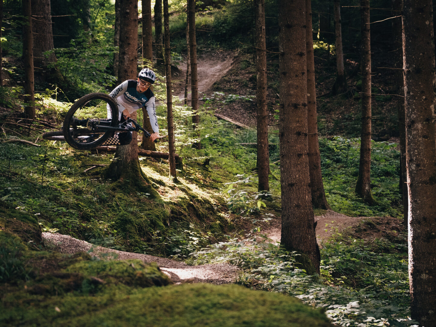 Mountainbiker im Wald springt über einen Sprung in die Luft.