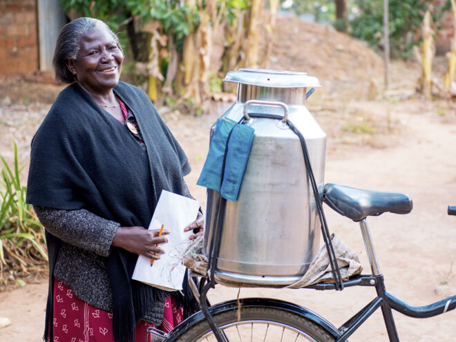 A dairy farmer smiling and standing next to her Buffalo Bicycle loaded up with a milk jug.