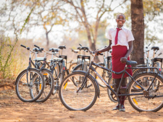 A smiling girl in her school uniform stands behind a Buffalo Bicycle with a row of bikes behind her.