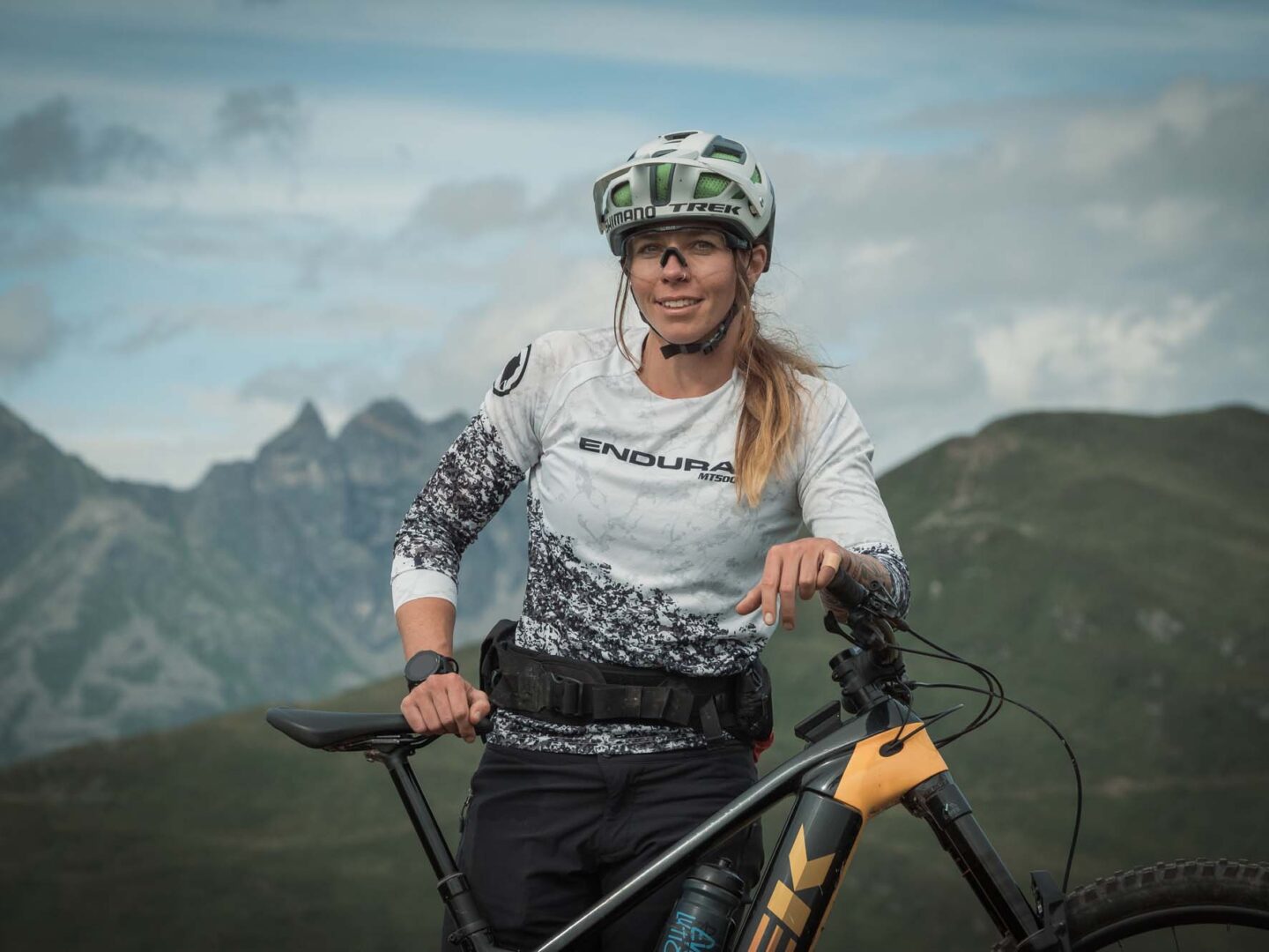 Frau steht hinter ihrem E-Mountainbike, im Hintergrund Natur und Berge